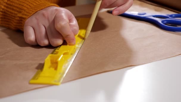Нерозпізнана жінка малює лінію ручкою, використовуючи лінійку на крафт-папері крупним планом — стокове відео