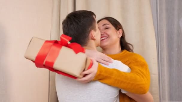 Um casal feliz a abraçar-se. Mulher segurando presente com fita vermelha — Vídeo de Stock