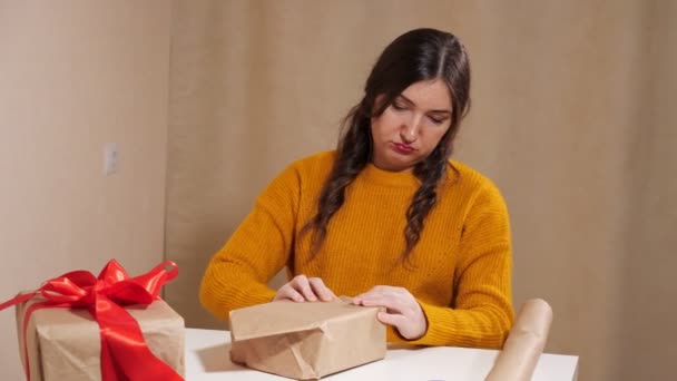Mujer joven molesta tratando de envolver el regalo en papel kraft — Vídeos de Stock