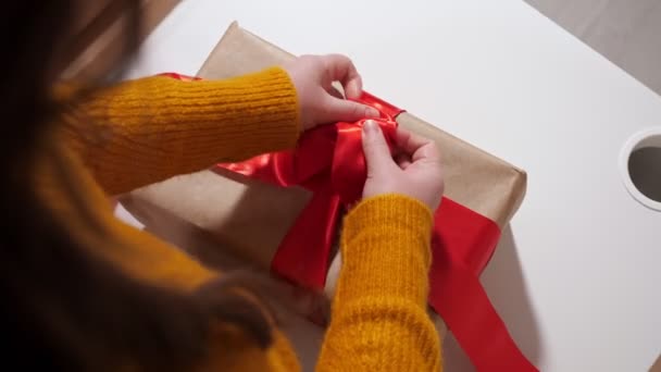 Неузнаваемая женщина завязывает подарочную коробку красной лентой, вид сверху — стоковое видео