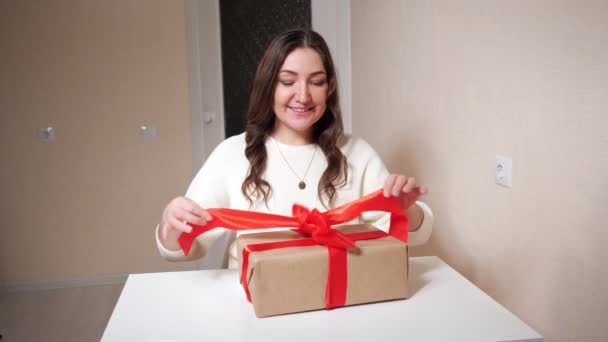 Hermosa mujer morena desempaca un regalo sentado en la mesa — Vídeos de Stock