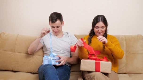 Mooi stel man en vrouw open geschenken zittend op de bank. De mens is gelukkig. — Stockvideo