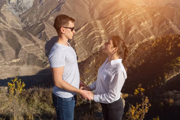 Мужчина и женщина стоят напротив друг друга, держась за руки на фоне гор, солнечного света — стоковое фото
