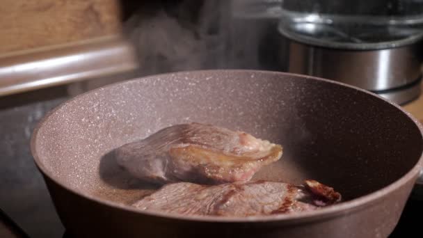 Dos filetes de carne se fríen en una sartén de vapor se eleva en cámara lenta — Vídeos de Stock
