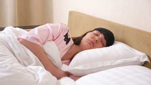 Молода жінка в сплячій масці лежить розслаблена в сучасному ліжку — стокове відео