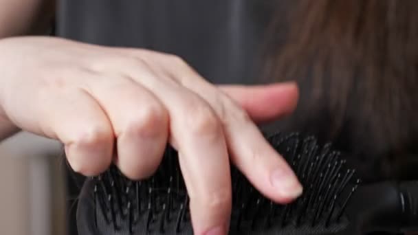 Jonge vrouw hand trekt lang donker haar uit borstel borstels — Stockvideo