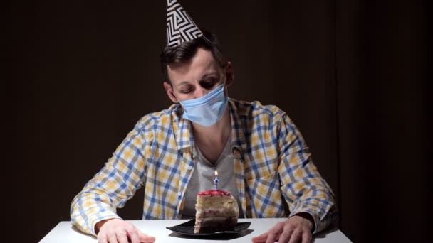 Homem perturbado em chapéu de festa e máscara descartável apaga vela — Vídeo de Stock