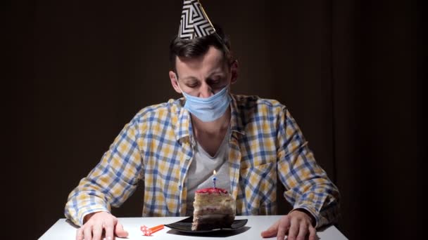Парень в маске и цветной шляпе на день рождения дует на свечи — стоковое видео