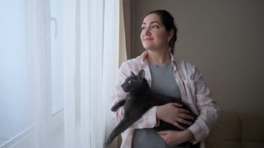 Pencereden dışarı bakan kedili genç bir kadın.