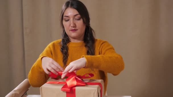 Fiatal nő díszíti ajándék doboz kötött piros szalag íj — Stock videók