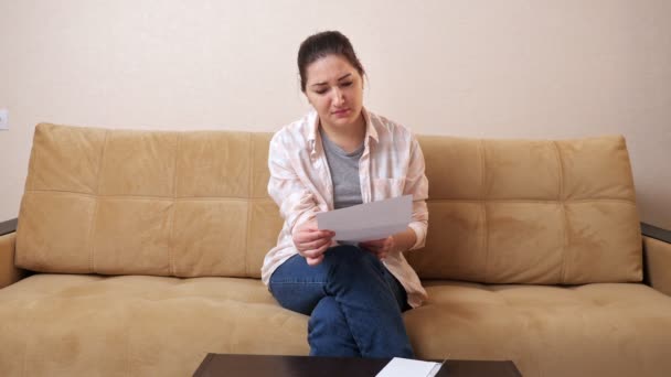 Mulher abre envelope com conta e fica nervosa no sofá — Vídeo de Stock