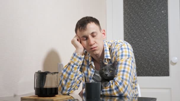 Schläfriger Mann sitzt mit grauer Katze am Tisch in der Küche — Stockvideo