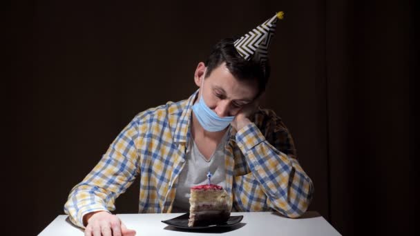 Расстроенный человек в шляпе и одноразовой маске задувает свечу — стоковое видео