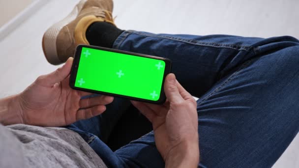 Onherkenbare man die op een stoel zit en een telefoon vasthoudt met een groen scherm — Stockvideo