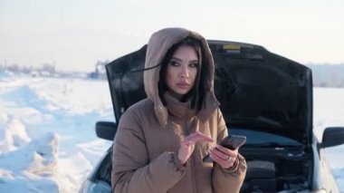 Telefonlu bir kadın bozuk arabanın yanında çekici bekliyor.