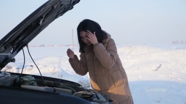 Rozrušená žena se dívá na rozbité auto motor na zasněžené silnici — Stock video