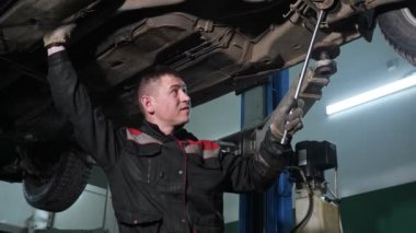 Genç çalışan, istasyonda kırık otomobilin altını kontrol ediyor.