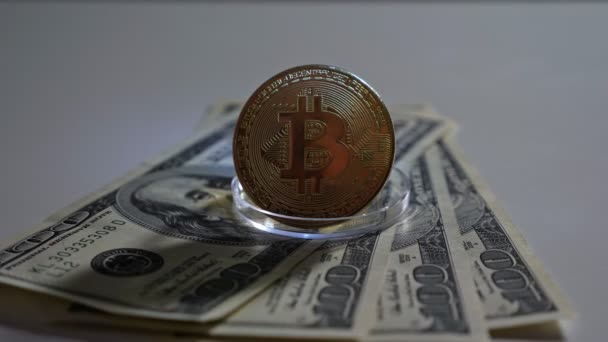Bitcoin de oro en un soporte se encuentra en billetes de dólar sobre un fondo blanco — Vídeos de Stock