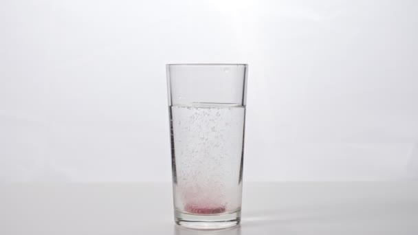 Compressa effervescente cade in un bicchiere d'acqua su uno sfondo bianco — Video Stock