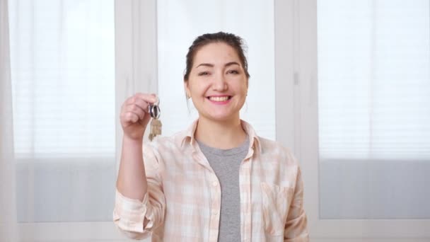 Radosna kobieta potrząsa nowymi kluczami stojąc przy oknie — Wideo stockowe
