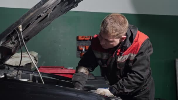Üniformalı genç işçi bozuk otomobili tamir etmek için muayene ediyor. — Stok video