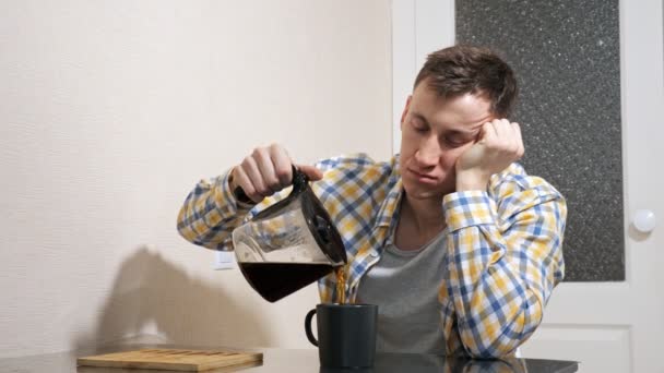 Schläfriger Mann schenkt Kaffee ein, während er am Tisch in der Küche sitzt — Stockvideo