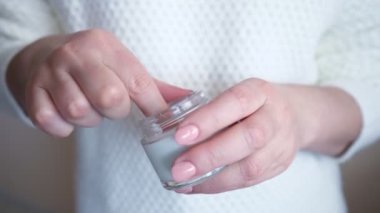 Beyaz kazaklı tanınmayan bir kadın cam kavanozdan krem sürüyor.