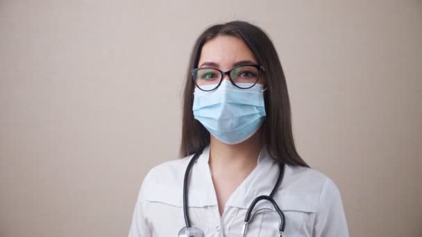 Bej arka planda gözlüklü ve maskeli bir doktor. — Stok video