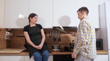 Adam tavada krep çeviriyor ve bir kadın masada oturuyor.