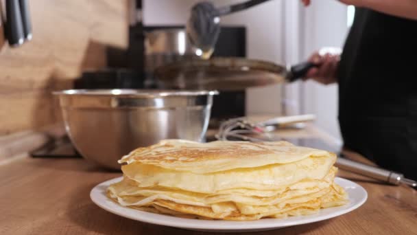 Стопка млинців на тлі невпізнаваної жінки, що наливає тісто на сковороду — стокове відео