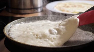 Tanımlanamayan bir kadın, spatulayla yakın plan bir tavada krep çeviriyor.