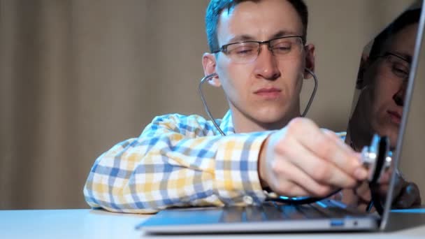 Man with glasses diagnoses a laptop using a phonendoscope — Stock Video