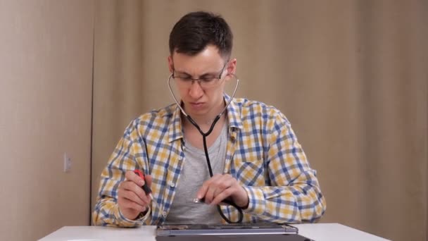 Hombre con gafas examina un portátil desmontado y escucha con un fonendoscopio — Vídeos de Stock
