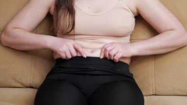 Spor kıyafetli tanınmayan bir kadın koltukta otururken göbeğine dokunuyor.
