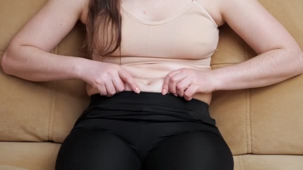 Mulher irreconhecível em sportswear tocando gordura da barriga enquanto sentado no sofá — Vídeo de Stock