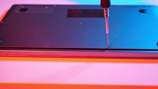 Unrecognizable master screwing bolts into laptop lid in muted red and blue light — Stock Video