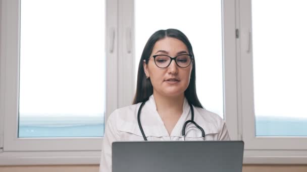 Жінка консультує пацієнта через відеозапис на ноутбуці в офісі — стокове відео