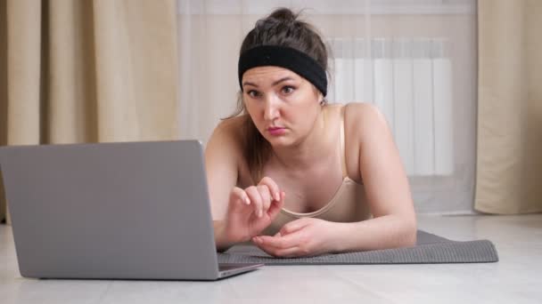Brunette femme faire de l'exercice dos tout en étant couché sur le tapis et en regardant dans un ordinateur portable — Video