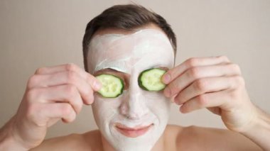 Yüzünde maske olan genç adam gözlerini kapatan salatalıkla oynuyor.