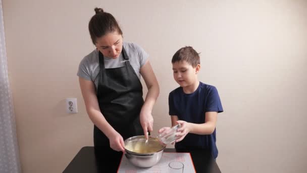 Chlapec nalévá mouku do těsta, zatímco žena mísí s whisk — Stock video