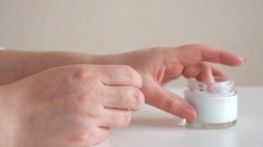 Tanınmayan bir kadın cam bir kavanozdan ellere krem sürüyor.