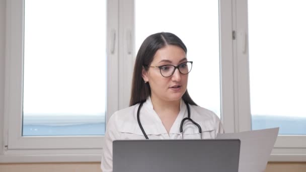 Il dottore femminile con occhiali e stetoscopio consulta il paziente in linea con computer portatile — Video Stock