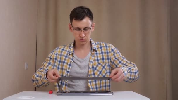 Mann mit Brille zerlegt Laptop, während er an weißem Tisch sitzt — Stockvideo