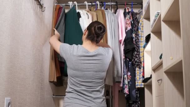 Senhora triste tenta encontrar roupas elegantes no armário walk-in — Vídeo de Stock