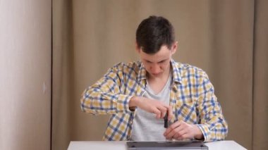 Genç adam masada otururken bir dizüstü bilgisayarı tornavidayla söküyor.