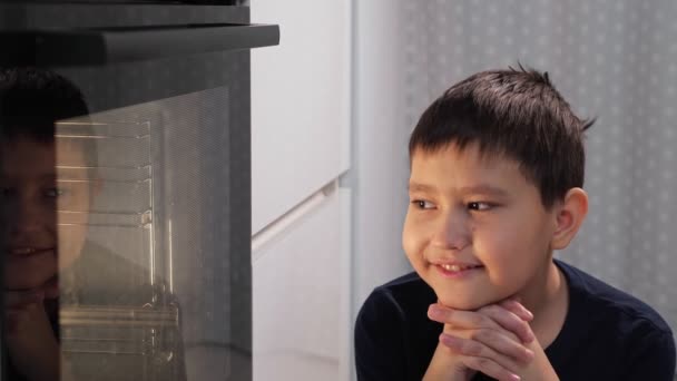 Boy sits and looks at the oven while waiting for the dish — Stock Video