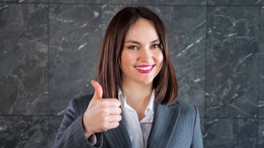 Kısa siyah saçlı, gülümseyen ve baş parmağını kaldıran genç bir kadın.