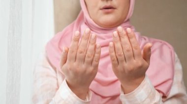 Tanımlanamayan pembe tesettürlü kadın önünde el ele tutuşan ve yüzünü yıkayan bir dua okuyor.