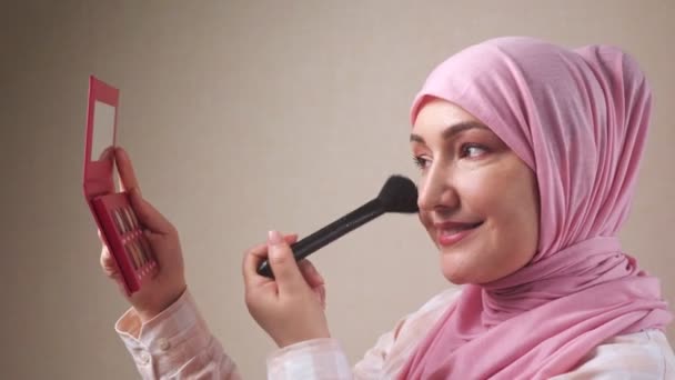 Vrouw in hijab het aanbrengen van make-up met een borstel terwijl kijken in de spiegel — Stockvideo