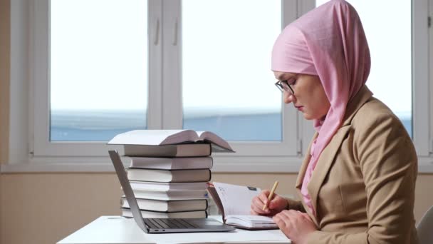 Wanita Muslim menulis dengan pena di notebook melihat ke dalam laptop, gerakan lambat — Stok Video